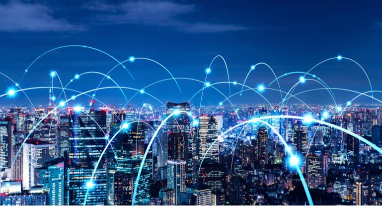 Nächtliche Skyline einer Großstadt, auf der die einzelnen Gebäude als Symbol für das LPWA-Roaming im IoT mit blauen Laserstrahlen verbunden sind