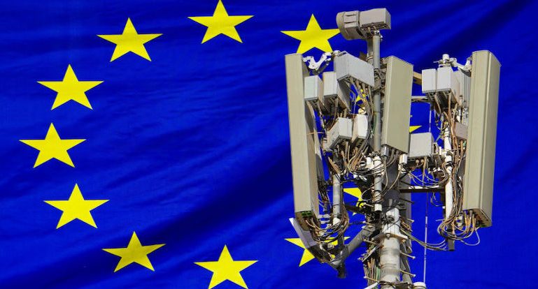 Der obere Teil des Sendemasts eines Telekommunikationsanbieters vor einer europäischen Flagge