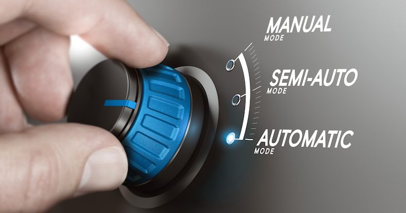 Hand turning a knob over grey background and selecting the automatic mode.